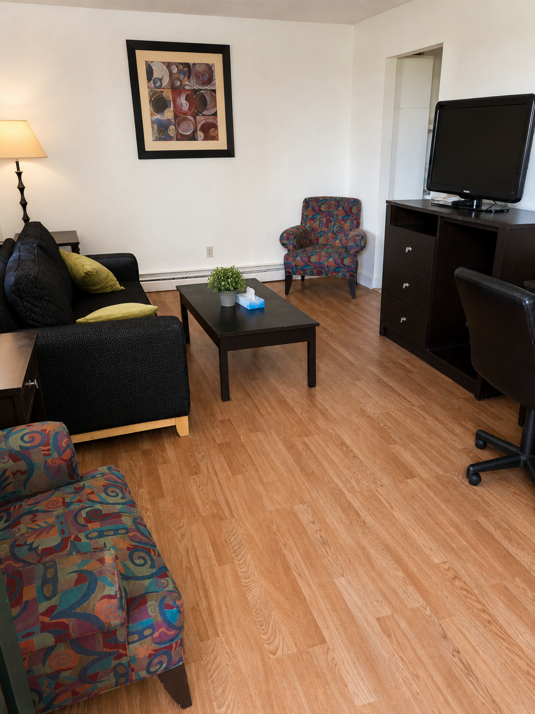 Furnished living area at Sunset Suites with sofa, accent chairs, coffee table, TV console and desk chair