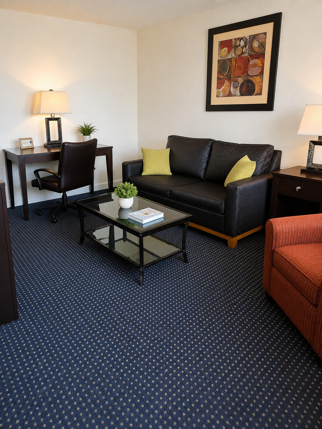 Furnished living room at Sunset Suites with a dark sofa, accent chair, glass coffee table and work desk