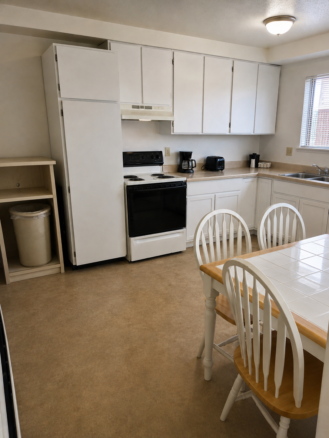 Full kitchen at Sunset Suites with refrigerator, range, coffee maker, toaster and tile-top dining table