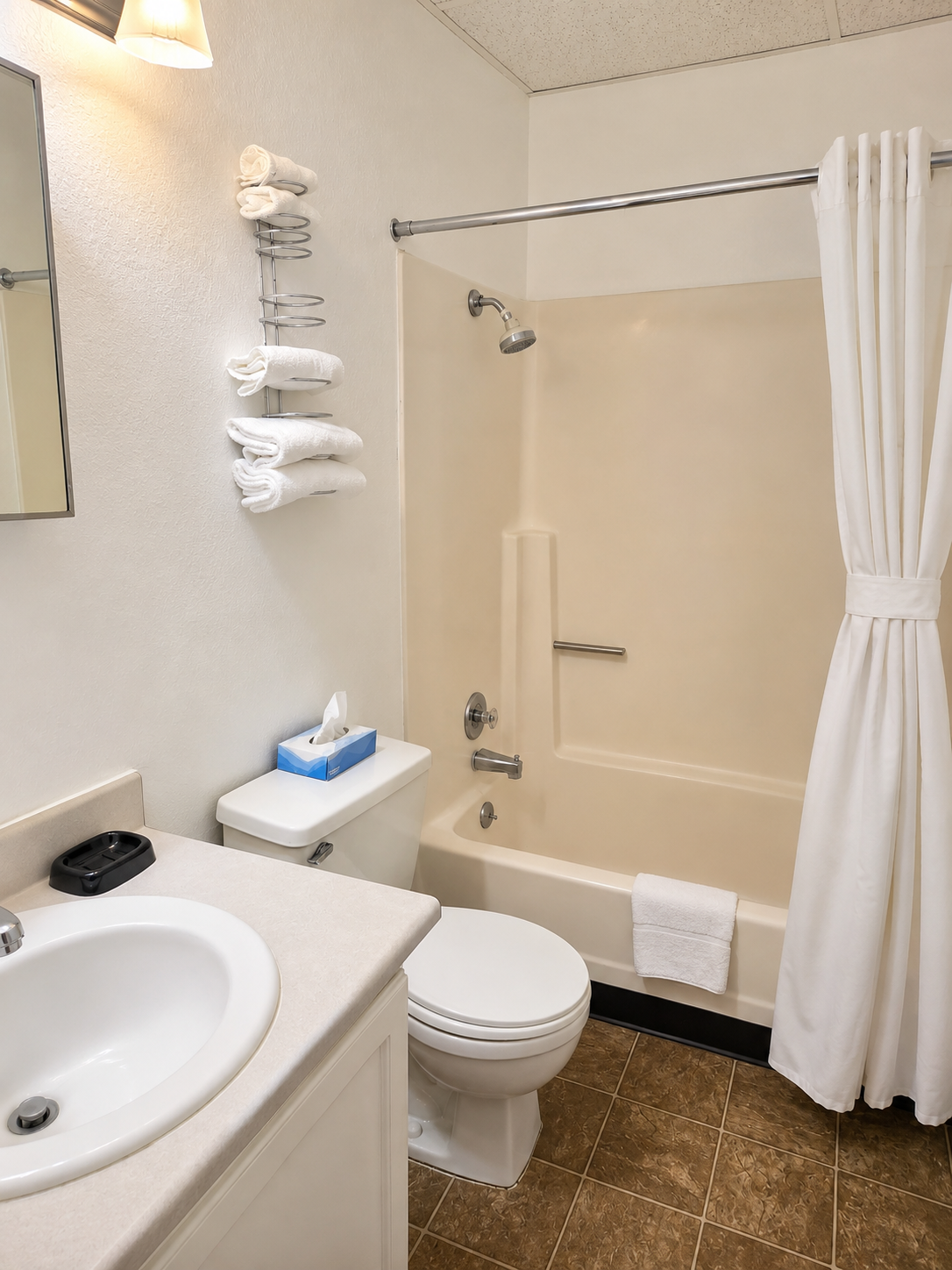 Clean full bathroom at Sunset Suites with tub and shower, vanity sink, mirror and stacked fresh towels